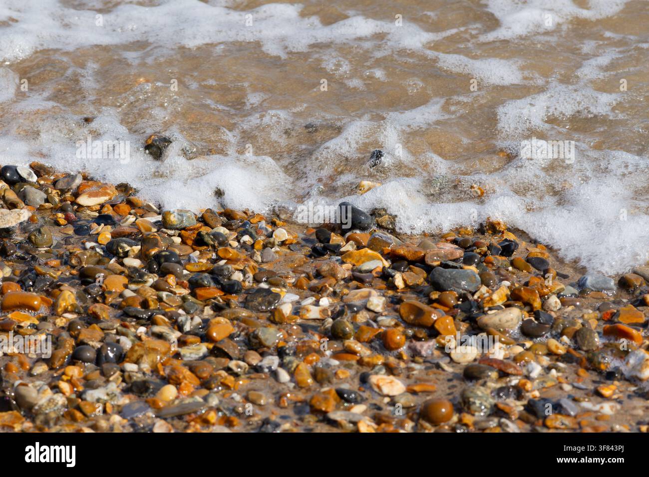 Nahaufnahme von schäumendem Meerwasser und Kieselsteinen an einem Strand Stockfoto