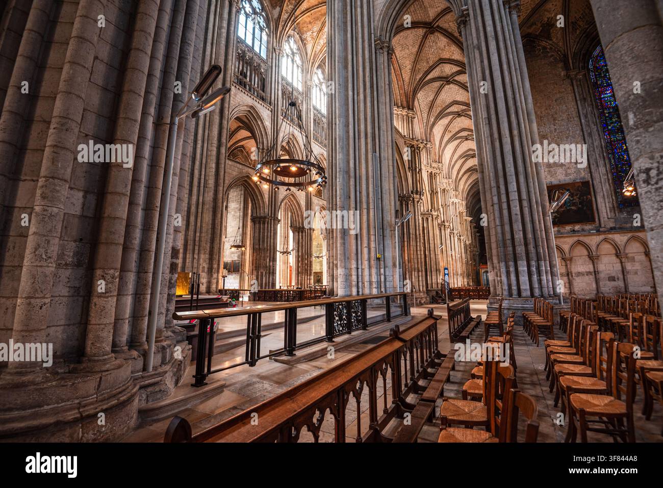 Erkundung des Seitenschiffs der Kathedrale von Rouen mit hohen Säulen, Kreuzrippengewölben und bleiverglasten Fenstern, die das Licht zeigen Stockfoto