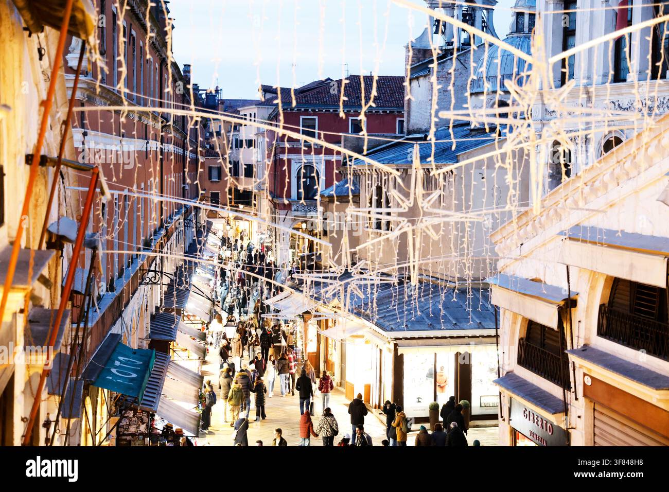 Straßenszene in der Dämmerung in Venedig mit Weihnachtslichtern und lebhaften Menschenmassen auf engen Wegen, die mit Geschäften gesäumt sind Stockfoto