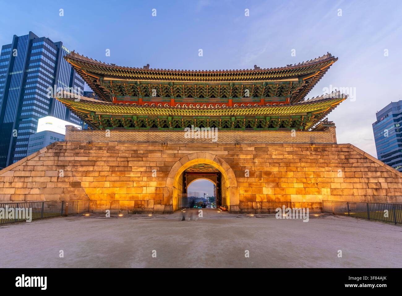 Ansicht des Sungnyemun-Tors bei Einbruch der Dunkelheit in Seoul mit Stadtlichtern und Architektur im Hintergrund Stockfoto