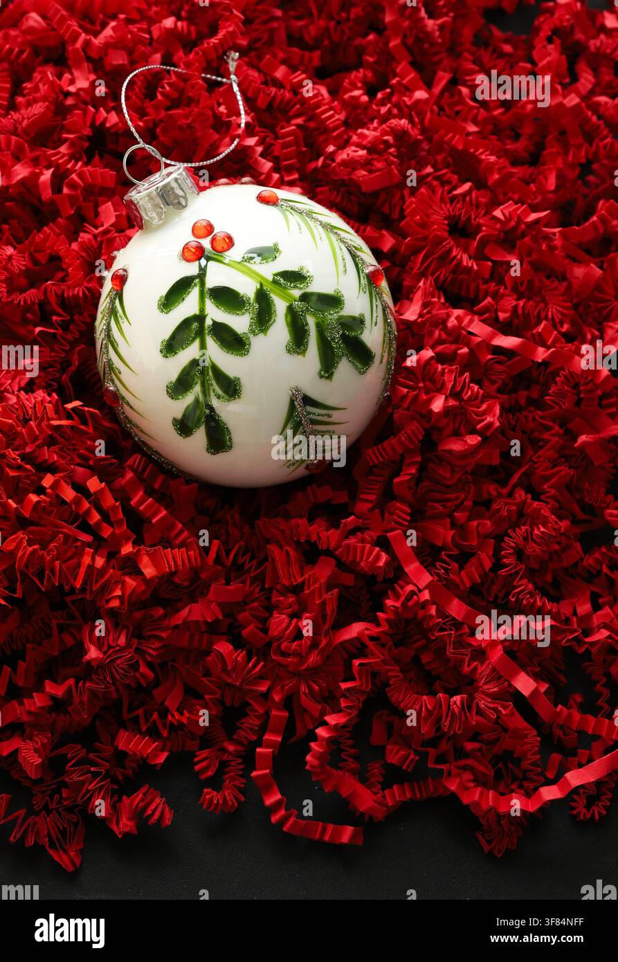 Eine weiße Glas-Weihnachtskugel mit grünem Mistelzweig auf rotem Hintergrund, symbolisch für den Weihnachtsgeist. Weihnachts- und Feiertagssaison. Stockfoto