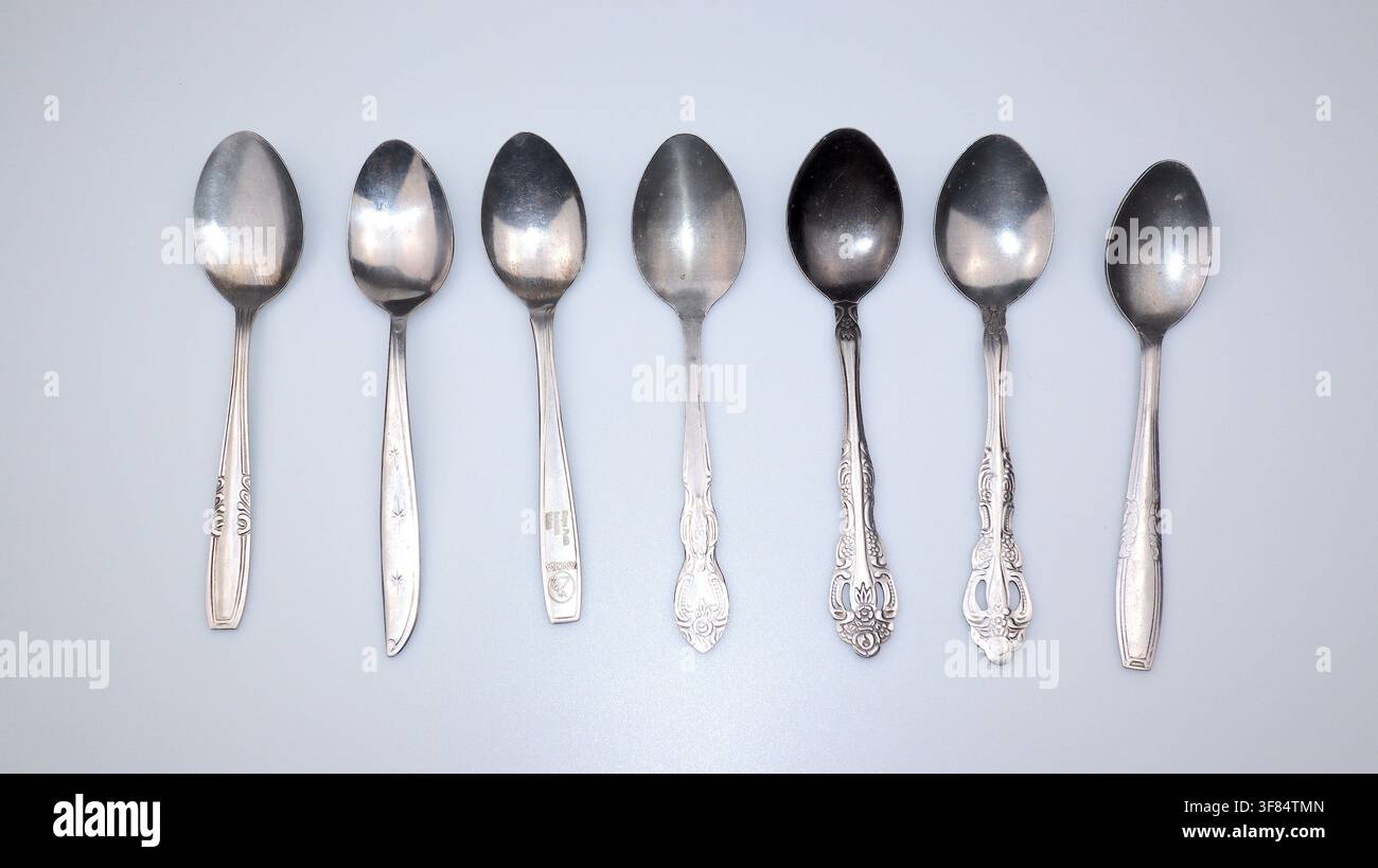 Verschiedene Metall-Teelöffel in einer Reihe angeordnet, isoliert auf weißem Hintergrund für Küchen-, Ess-, Kaffee-, Tee- und Geschirrkonzepte. Stockfoto