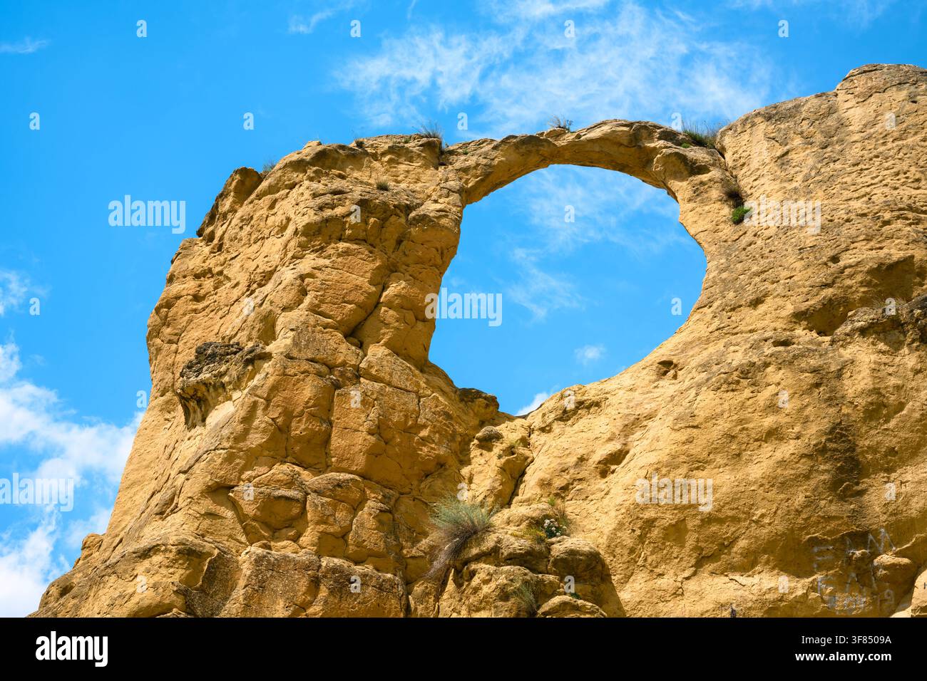 Eine große, natürliche Sandstein-Felsformation mit einem markanten runden Loch oder Bogen in ihrer Mitte. Der raue, hellbraune Fels ist mit Rissen texturiert Stockfoto