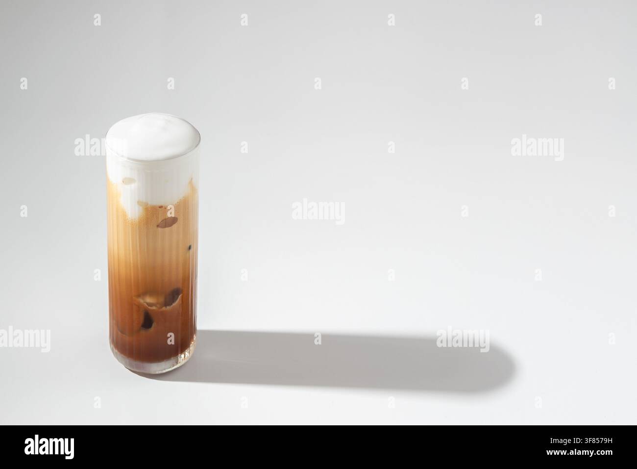 Eiskaffee mit cremiger Schaumkrone in hohem Glas auf weißem Hintergrund mit langem Schatten Stockfoto