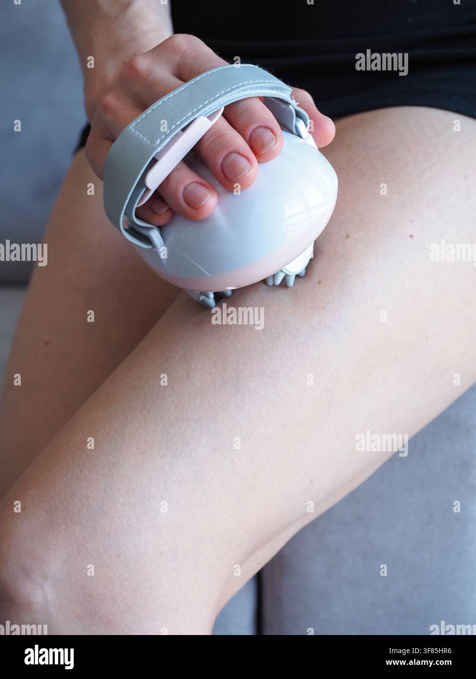 Reife Frau verwendet einen tragbaren elektrischen Massager am Oberschenkel zu Hause Stockfoto
