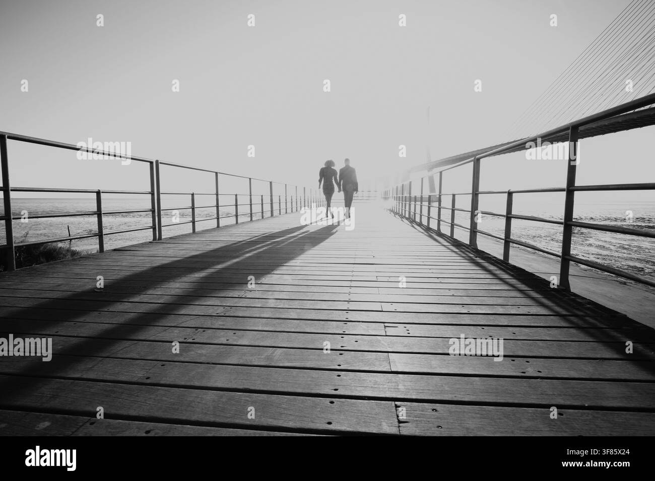Paar, das auf einem Holzsteg weggeht und lange Schatten im Nebel wirft Stockfoto