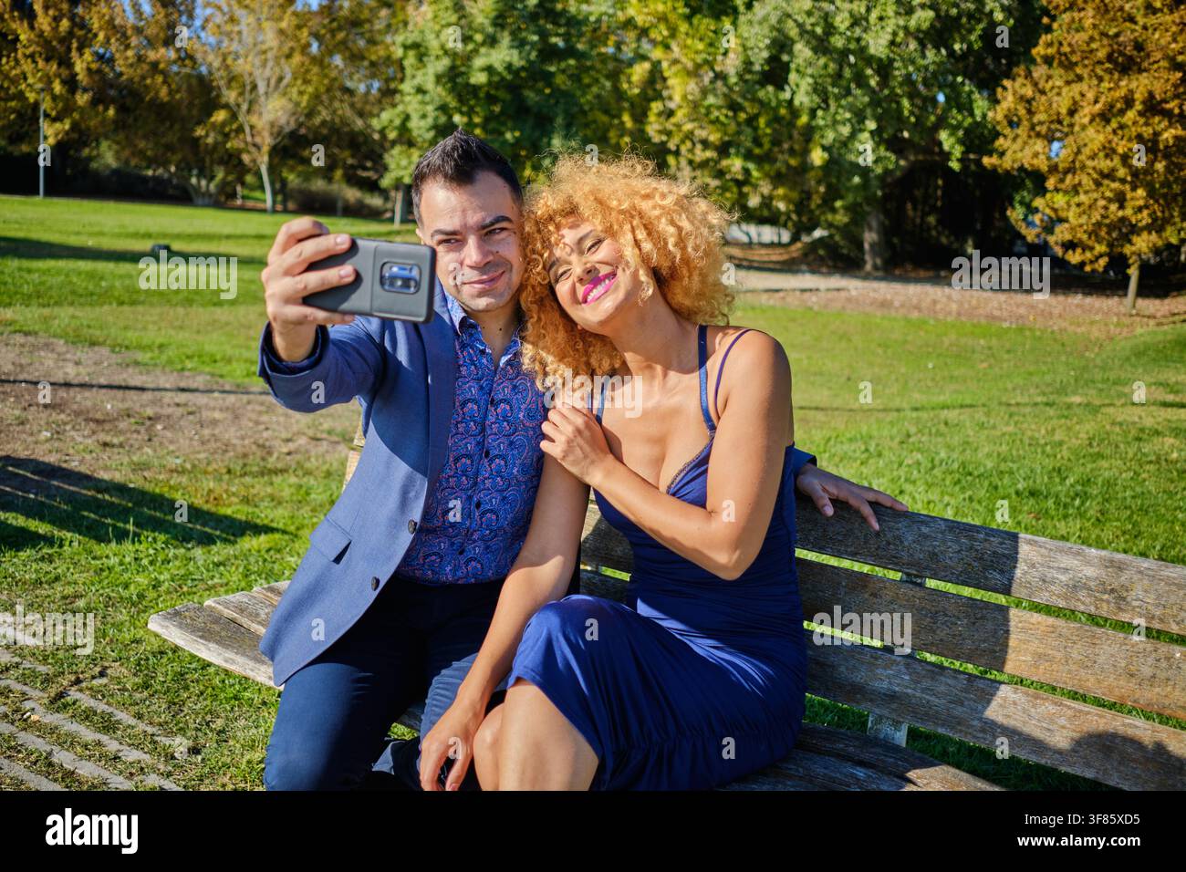Fröhliches Paar fängt einen Moment auf einer Parkbank mit einem Smartphone ein Stockfoto