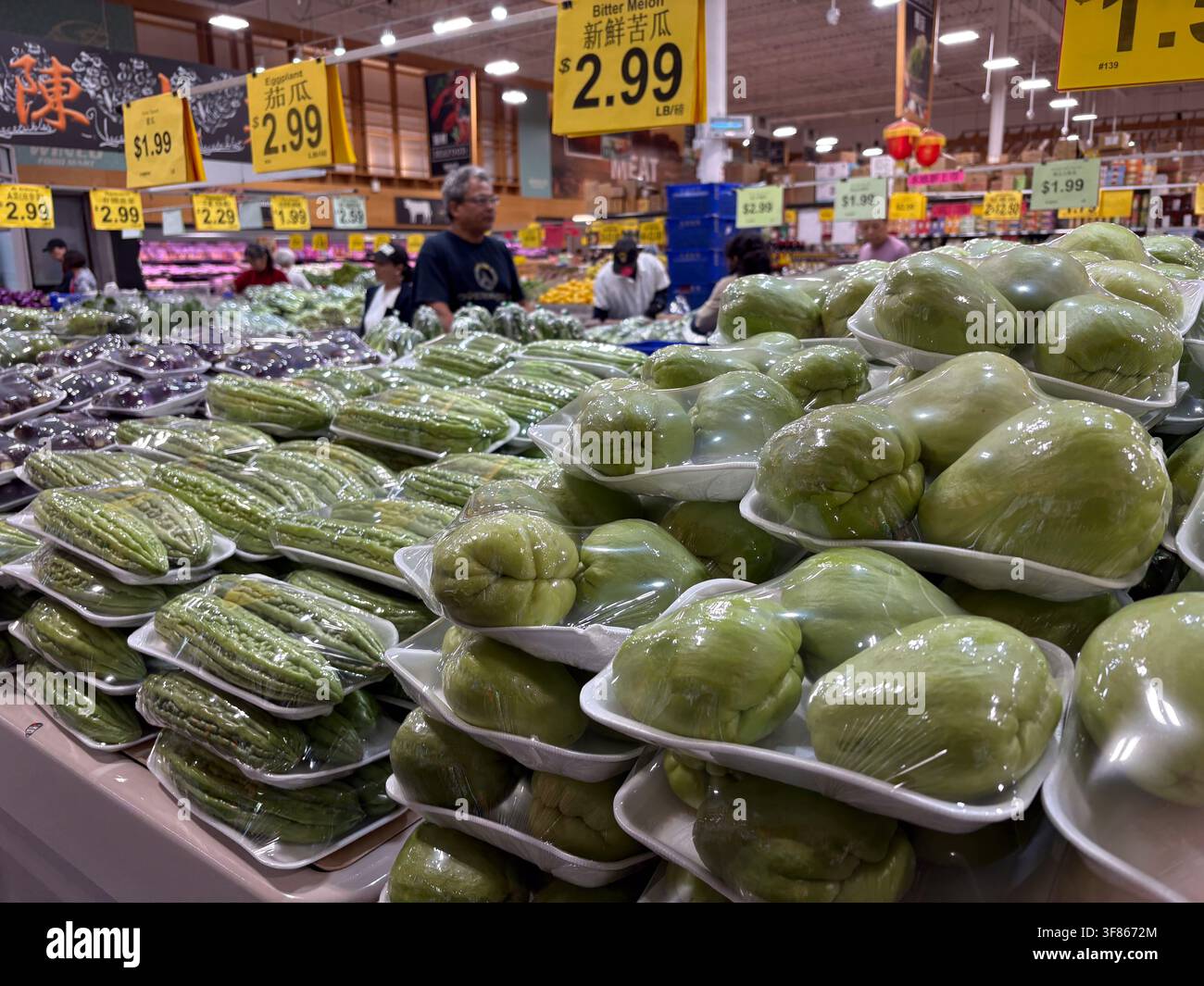 Obst- und Gemüsetheke in einem chinesischen Lebensmittelgeschäft mit verpackten Chayote-Kürbissen und Bittergurken auf den Regalen. Stockfoto