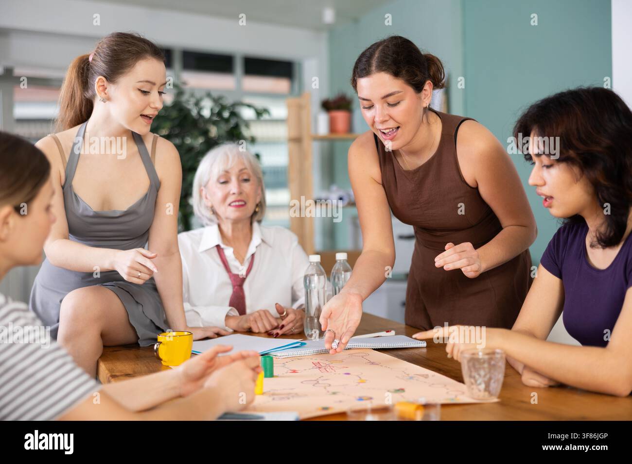 Glückliche Büroangestellte unterschiedlichen Alters verbringen Freizeit im Büro und spielen auf spielerische Weise logische Brettspiele und mentale Aktivitäten Stockfoto