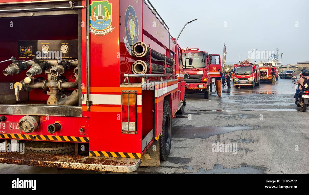 Rote Feuerwehrfahrzeuge und Feuerwehrleute auf nasser Straße in Indonesien Stockfoto
