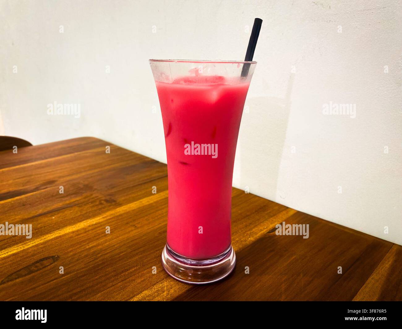Eisgetränk mit rosa Farbe und Strohhalm auf einem Holztisch in einem Café Stockfoto