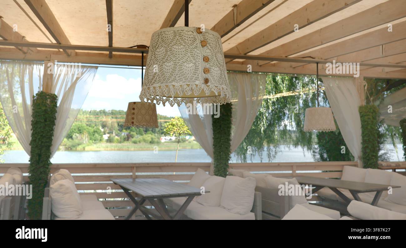 Lakeside-Restaurant-Veranda mit gemütlichem Boho-Innenarchitekturdesign. Modernes Öko-Tourismus-Gastgewerbe-Ressort-Entspannungskonzept. Ästhetische Uferpromenade-Terrasse Stockfoto