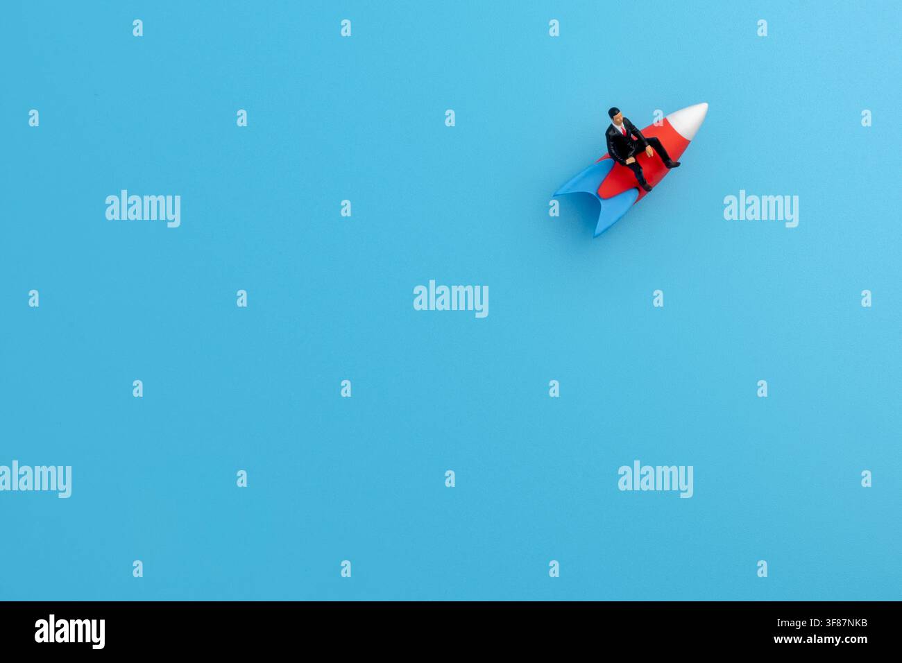 Miniatur-Geschäftsmann reitet auf einer rot-weißen Spielzeugrakete über einen blauen Hintergrund. Kopierraum für Text. Startup-Launch, Karrierewachstum Stockfoto