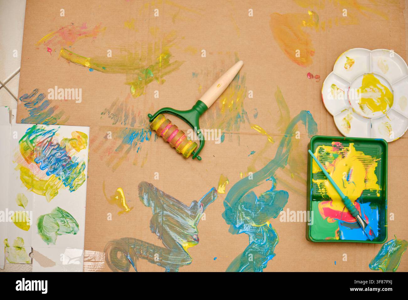 Kinder-Kunstbedarf und farbenfrohe Farbe, die ein kreatives Chaos auf braunem Karton erzeugen Stockfoto