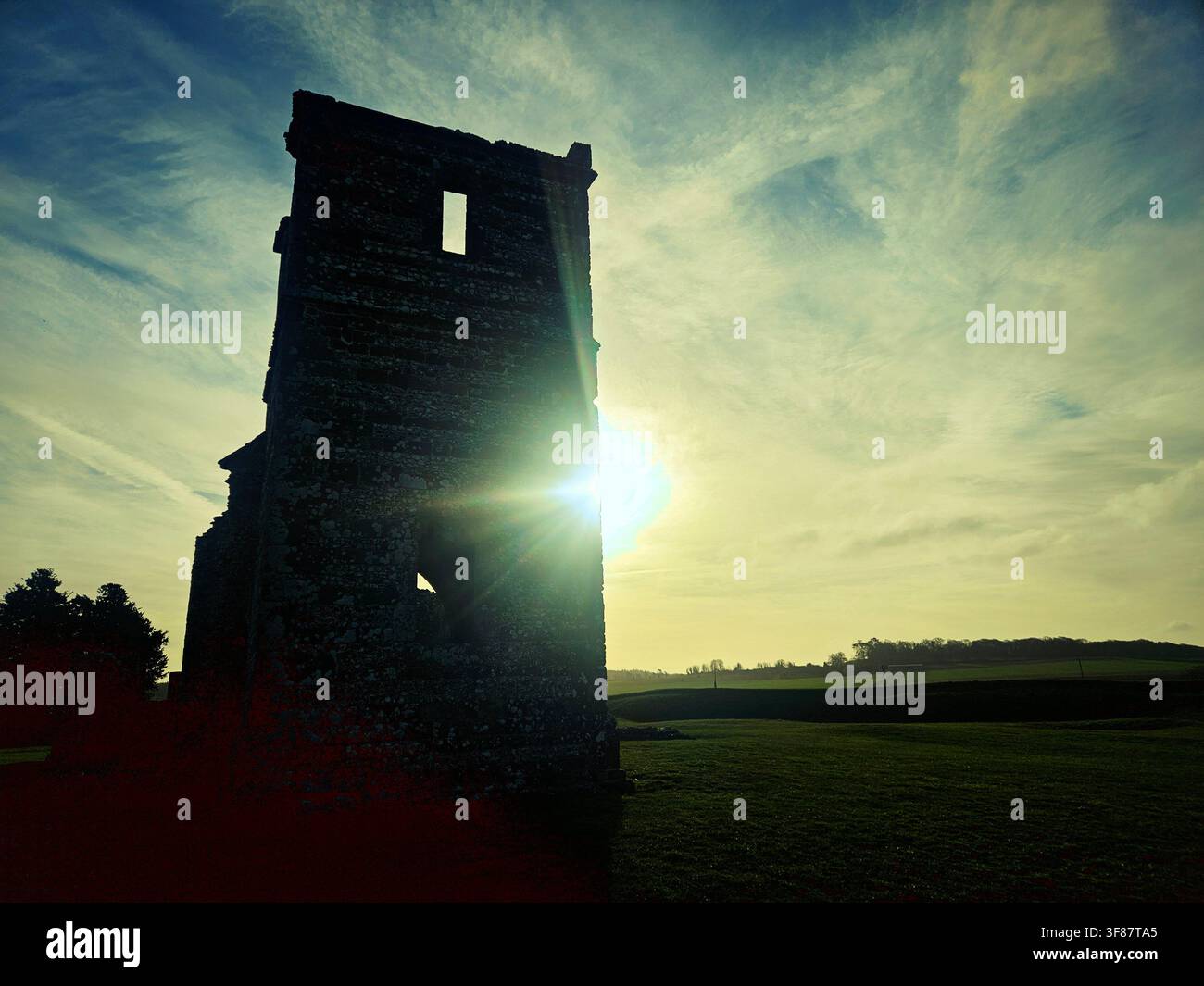 Die ruinierte Kirche von Knowlton aus dem 12. Jahrhundert bei Sonnenuntergang. Die normannische Kirche steht im Zentrum von Knowlton Henge, einem neolithischen Henge-Erdwerk nahe Wimborne Minster, Dorset, England, UK. Die Sonne scheint durch das Fenster des verfallenen Turms. Stockfoto