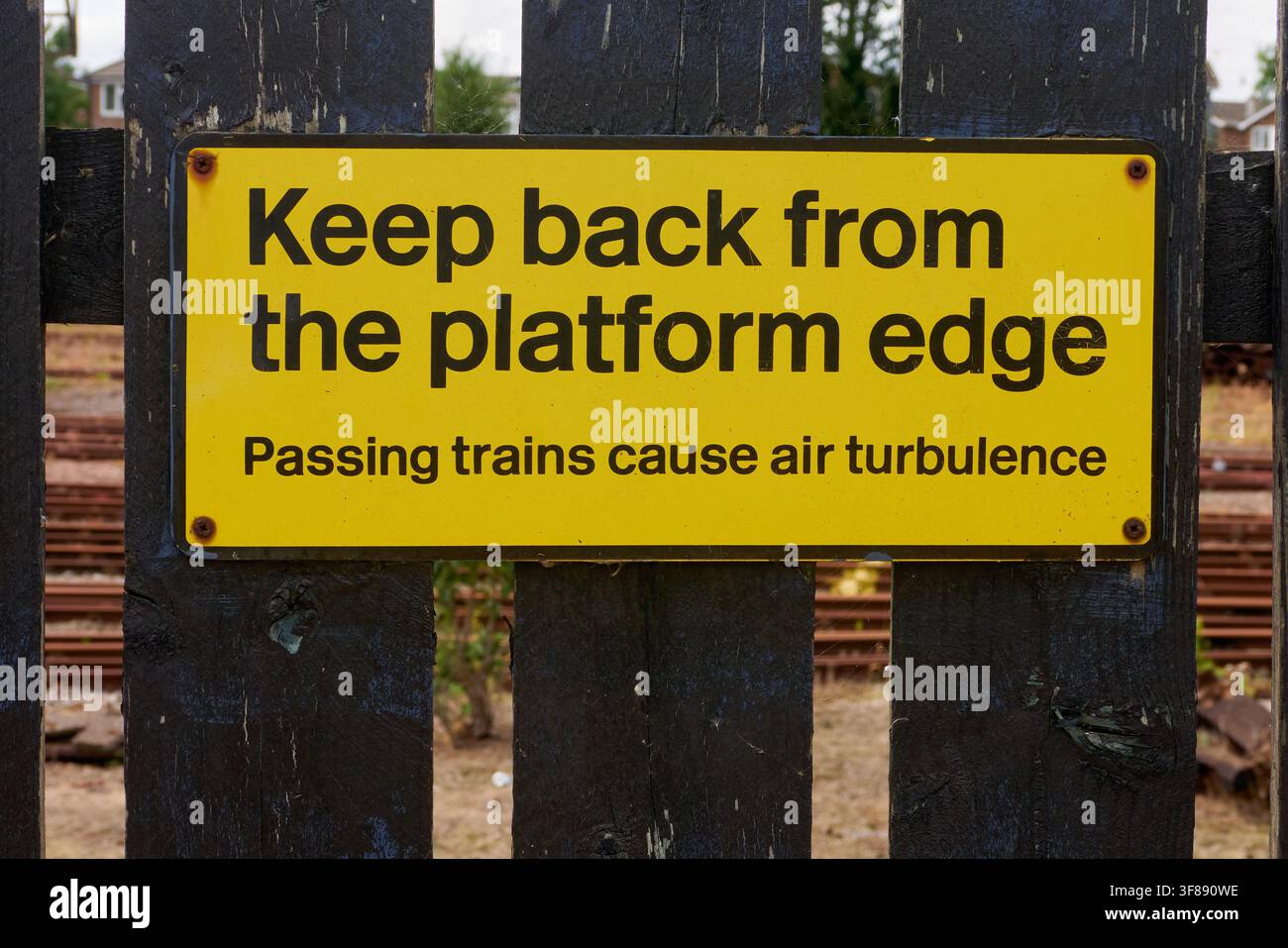 Hellgelbes Warnschild, Nahaufnahme, Abstand vom Bahnsteigrand halten. Vorbeifahrende Züge verursachen Luftwirbel. Modernes Grafikdesign, British Railways. Stockfoto