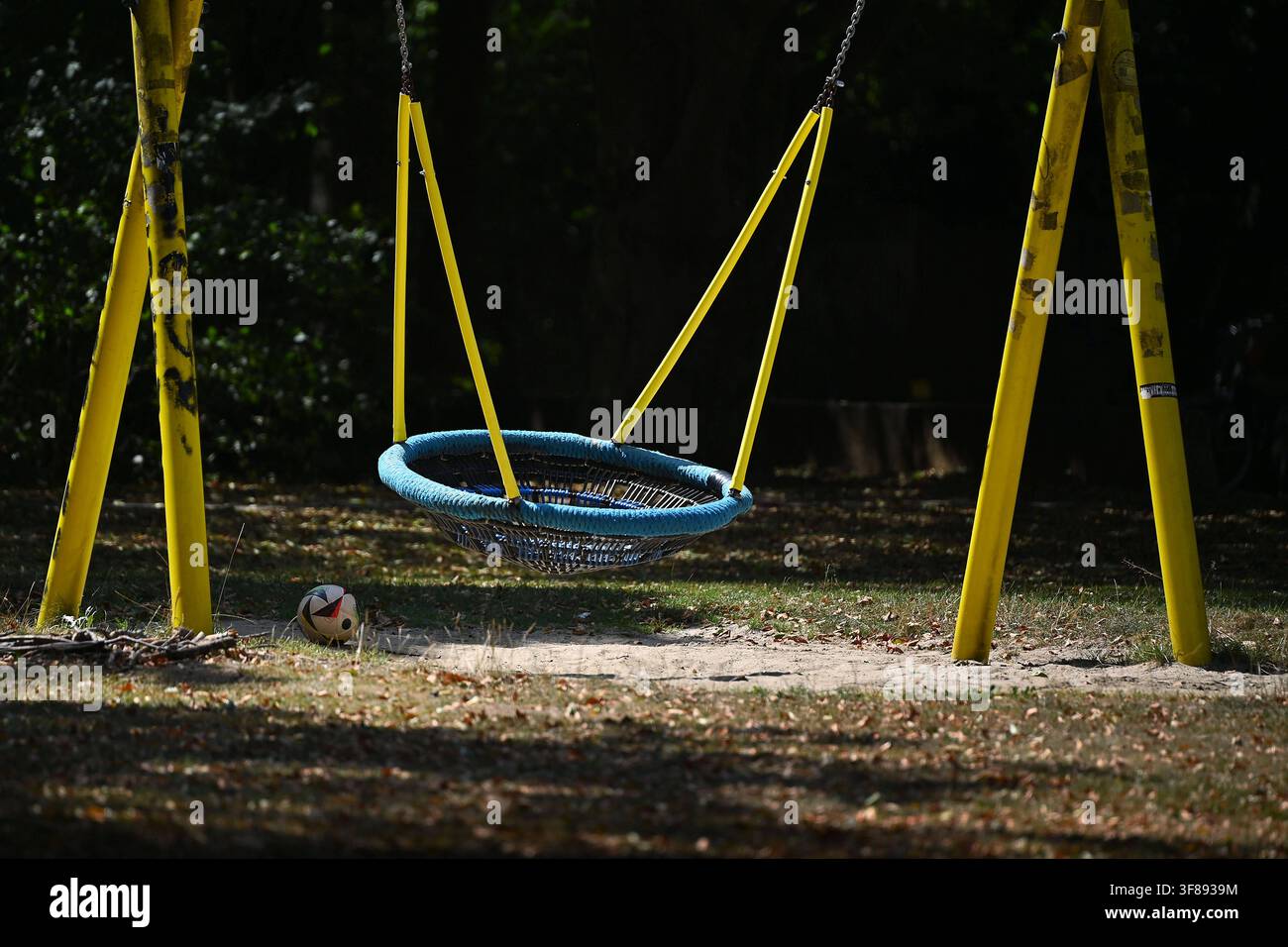 Leere große Korbschaukel im Park. Spielplatz im Grünen. Die Schaukel ist an einem gelben Metallgestell befestigt. Im Hintergrund sind dicht belaubte Bäume und eine schattige Parklandschaft zu sehen. Stockfoto