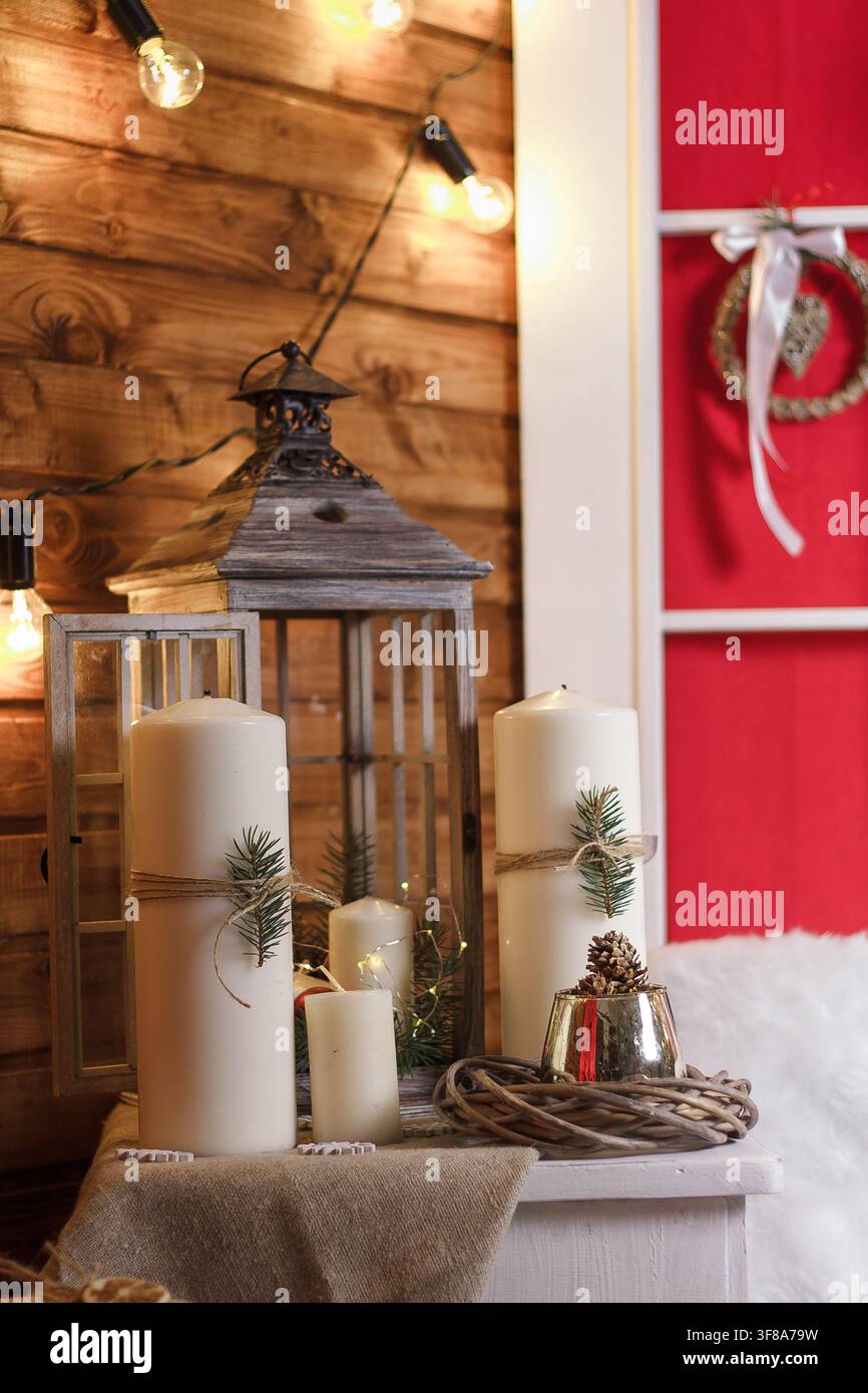 Weiße Kerzen und Weihnachtsdekoration mit Tannenzweigen, Zapfen und Kranz. Neujahr und Winterferienkonzept. Stockfoto