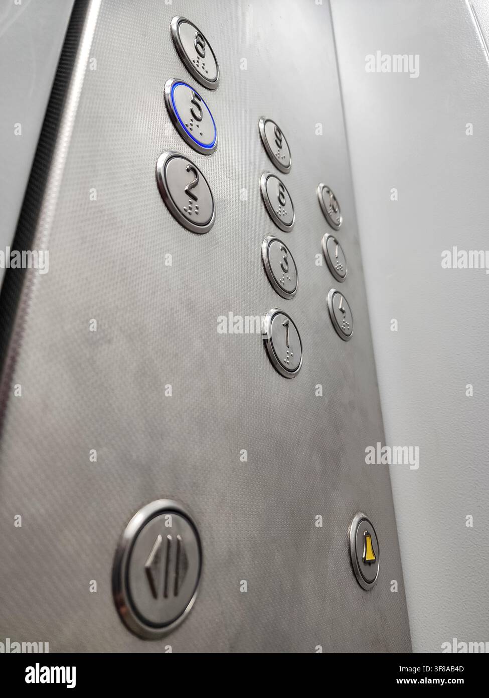 Edelstahl-Elevator-Steuerpanel mit beleuchteter "5"-Taste. Bezeichnung der Wahl des fünften Stockwerks. Neben numerischen Stockwerkstasten ein Stockfoto