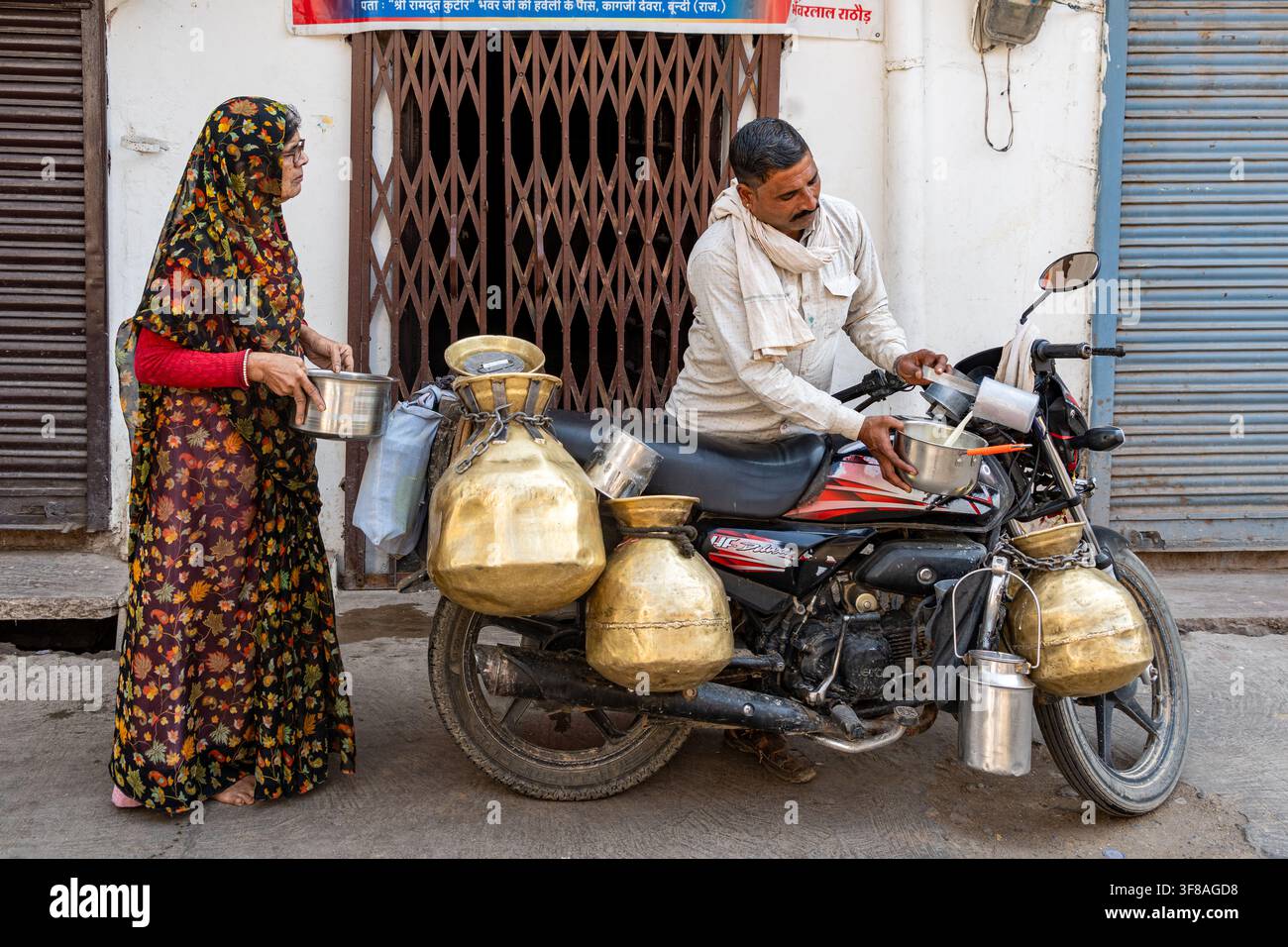 Indien. Rajasthan. Bundi. Ein Milchmann liefert Milch zu Hause aus, seitdem er auf seinem Motorrad mit Messingkantern beladen ist // Indien. Rajasthan. Bundi. Ein Milchmann liefert aus Stockfoto