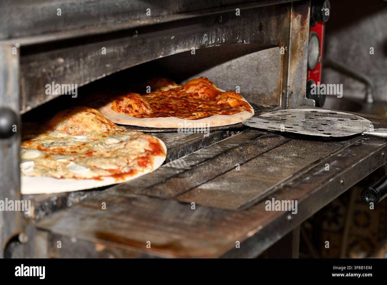 Zwei Pizzen im Ofen, eine fast fertig zum Herausnehmen, die andere noch nicht gebacken Stockfoto