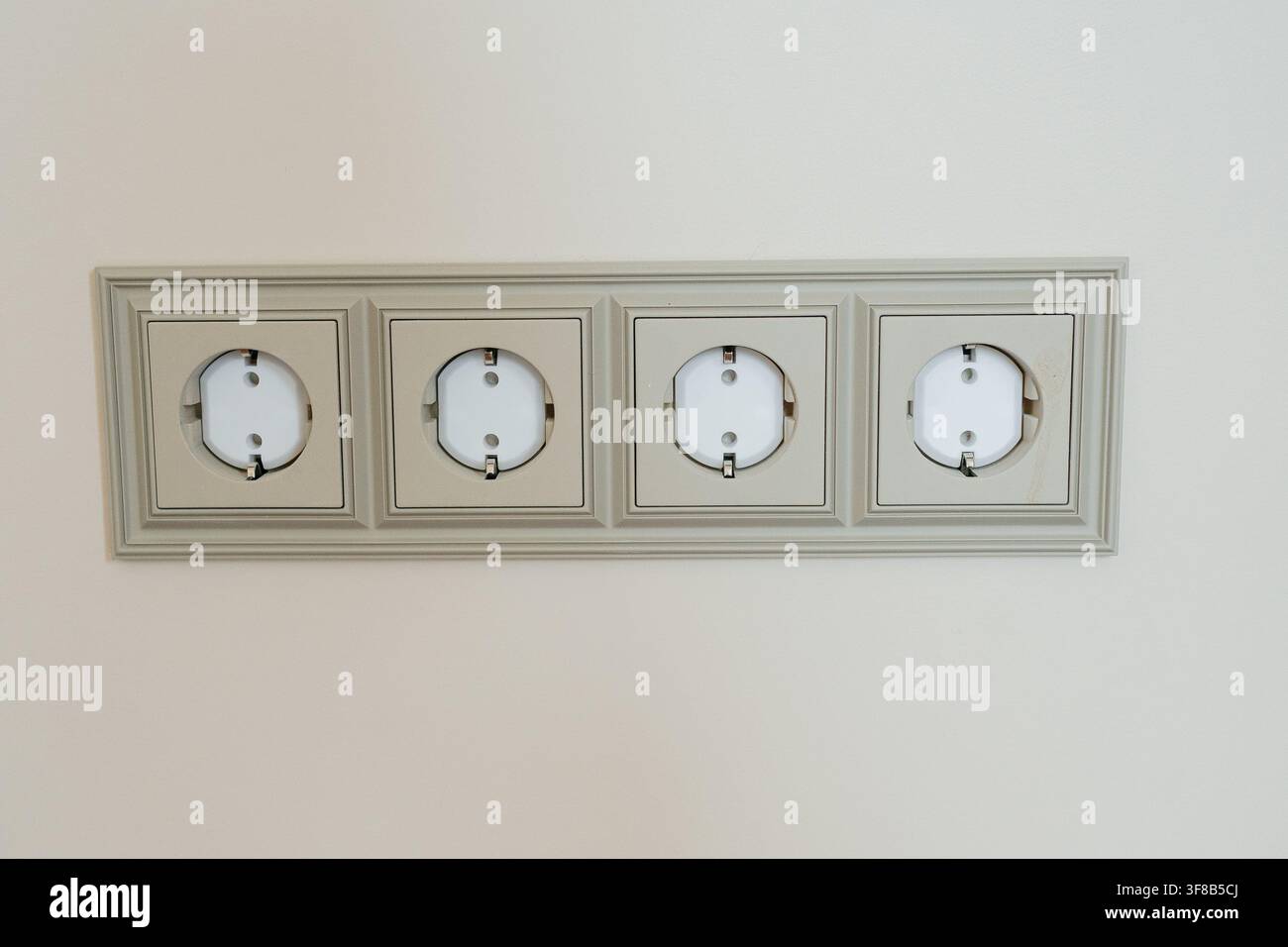Horizontalframe mit vier europäischen Erdstromsteckdosen, die an einer beigen Wand montiert sind. Perfekt für elektrische Installation, Hausautomation, Strom Stockfoto