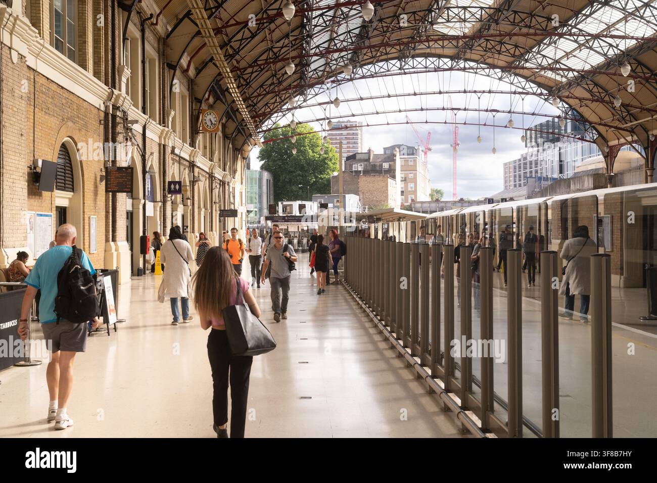 Pendler laufen entlang der Bahnsteige des historischen Paddington Bahnhofs in London unter seinem ikonischen viktorianischen schmiedeeisernen Bogendach. Stockfoto