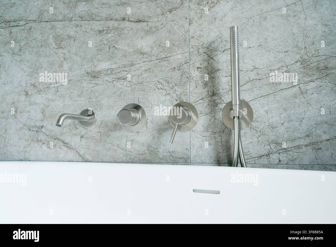 Nahaufnahme von modernen wandmontierten Badarmaturen und Auslauf mit einem hohen Handbrausestab in einem zeitgenössischen Badezimmer. Perfektes Stockfoto für Sanitär Stockfoto