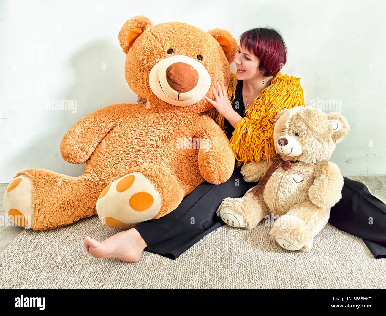 Junge Frau genießt einen verspielten Moment mit großen Teddybären in einer gemütlichen Inneneinrichtung Stockfoto