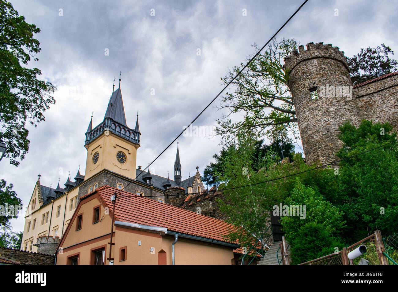 Gotischer Uhrturm und steinerner Festungsturm einer tschechischen Burg, der zwischen den Bäumen aufragt Stockfoto
