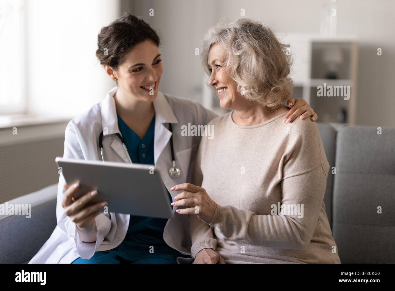 Ärztin konsultiert Seniorenpatienten zu Hause mit einem digitalen Tablet Stockfoto