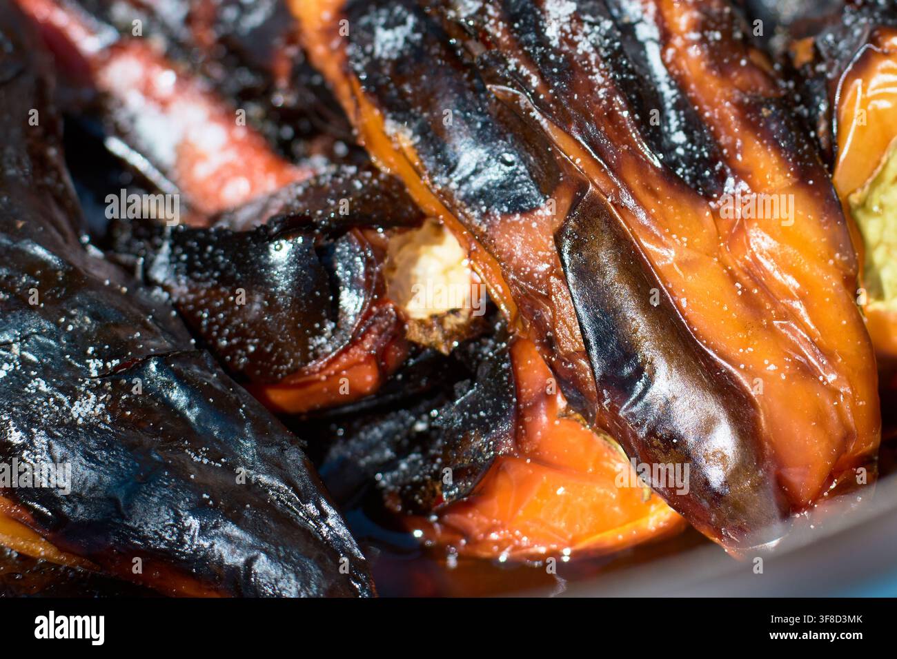 Nahaufnahme von frisch gegrillten Paprikaschoten mit verkohlter Haut und glitzernden Säften, großzügig mit groben Salzkrystallen in einer Kochpfanne gewürzt. Stockfoto