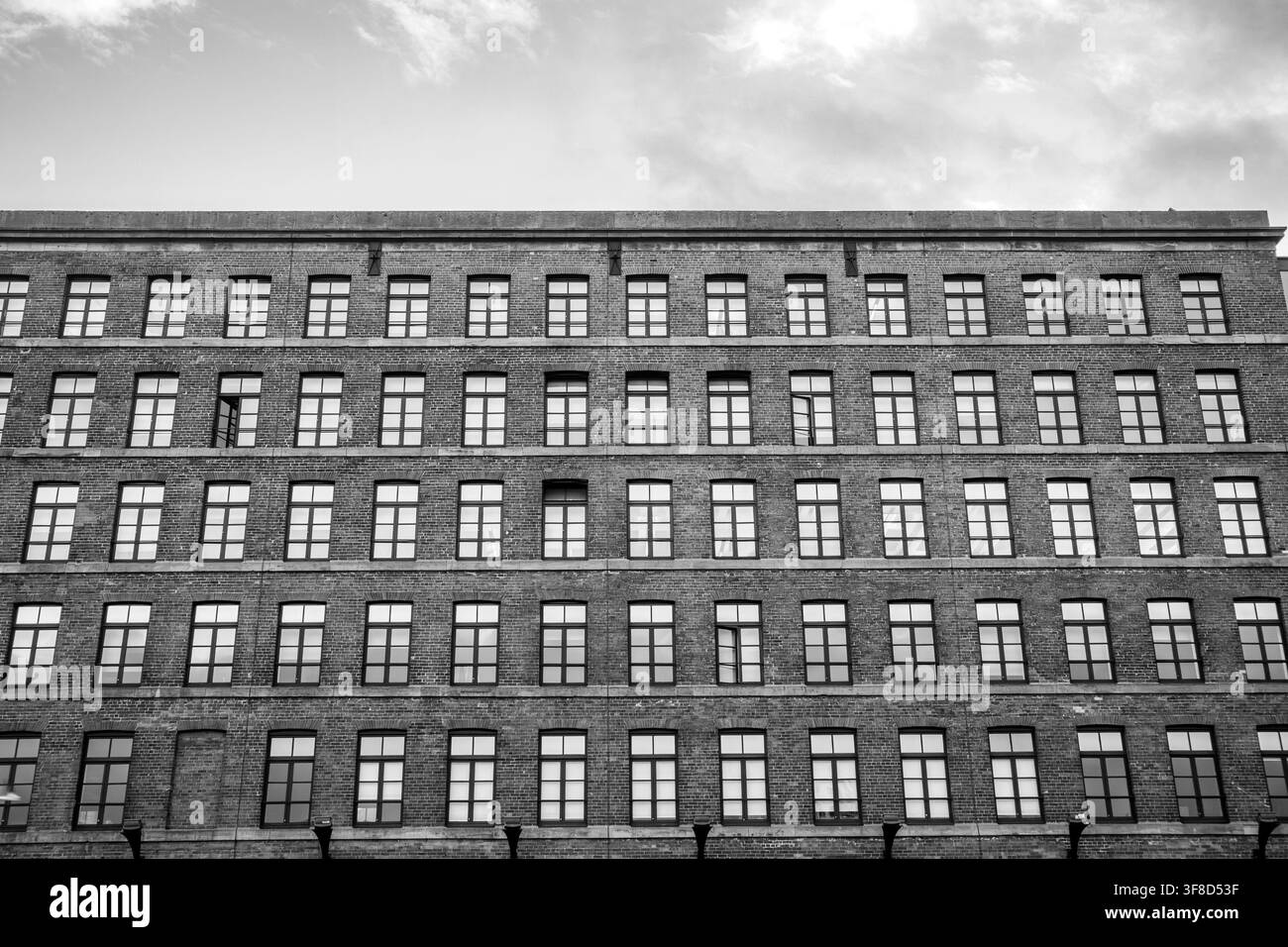 Schwarz-Weiß-Außenansicht, die das sich wiederholende Rastermuster der Fenster an der historischen Backsteinmühlenfassade zeigt, die zu Wohnungen umgebaut wurde Stockfoto