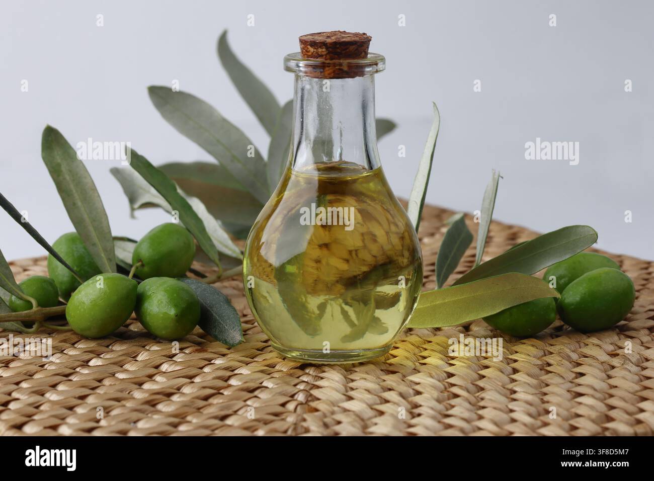 Glasflasche mit extra nativem Olivenöl mit grünen Oliven und Blättern Stockfoto