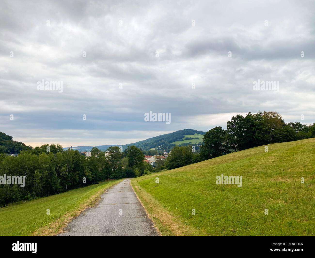 Pittoresker Wanderweg in einer Landschaft mit grünen Feldern und Dorfblick. Stockfoto