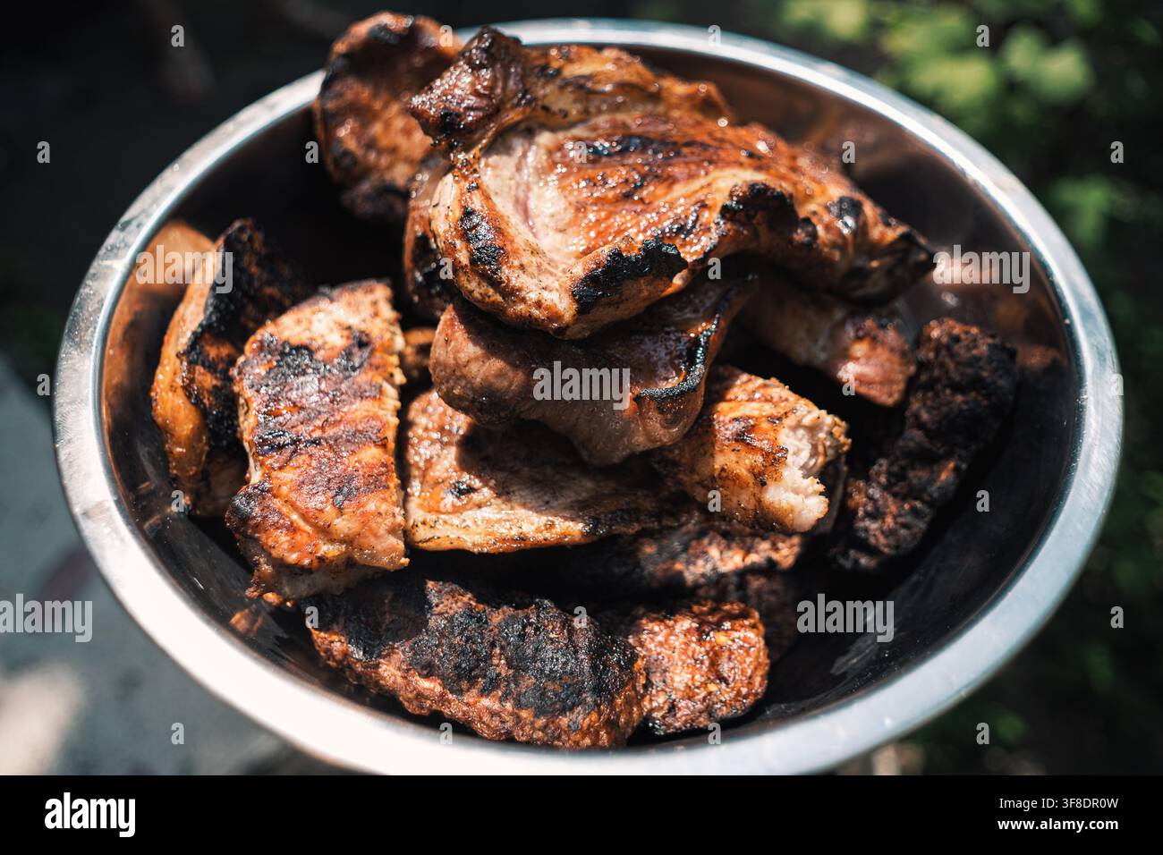 Nahaufnahme von frisch gegrillten Schweinefleischstücken, die nach dem Grillen über offenem Feuer in einer glänzenden Metallschüssel aufgeschichtet sind. Stockfoto