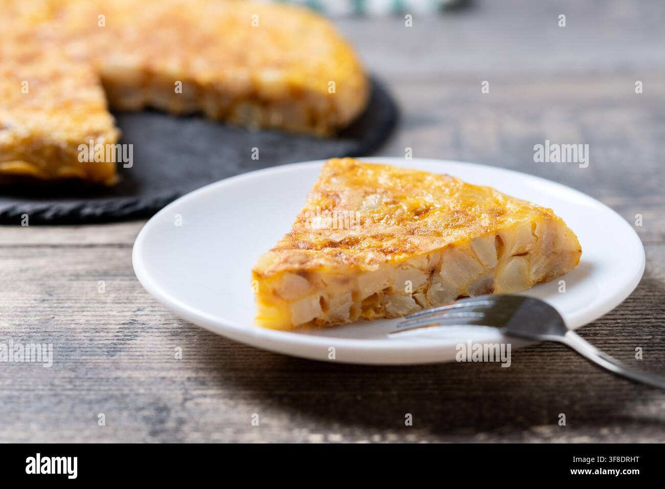 Scheibe traditionelles spanisches Kartoffelomelett aus Eiern und Kartoffeln, serviert auf einem weißen Teller mit einer Gabel auf einem rustikalen Holztisch. Stockfoto