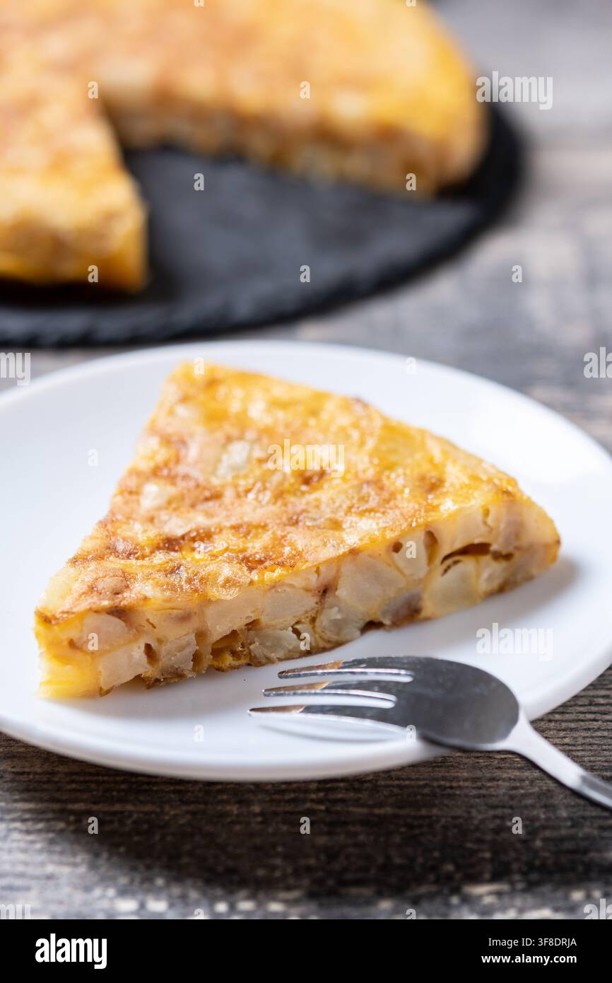 Scheibe traditionelles spanisches Kartoffelomelett aus Eiern und Kartoffeln, serviert auf einem weißen Teller mit einer Gabel auf einem rustikalen Holztisch. Stockfoto