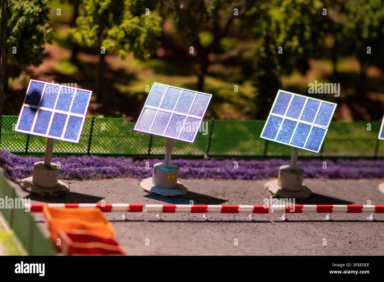 Drei kleine Solarmodell-Paneele stehen neben einer gepflasterten Straße in einer Miniatur-Landschaftsszene mit Bäumen und Zäunen. Stockfoto