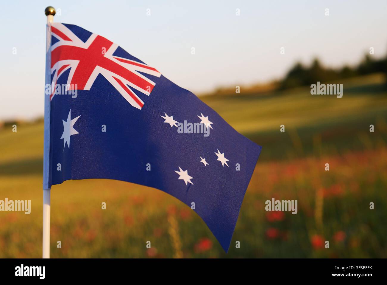 Australische Flagge weht vor einem Sonnenuntergangshimmel über einem Feld Stockfoto