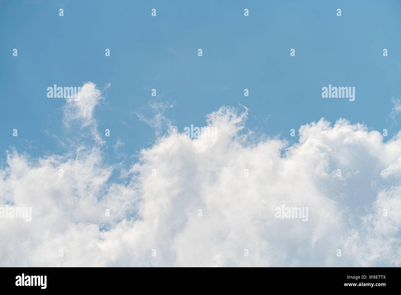 Flauschige Wolken ziehen langsam an einem strahlend blauen Himmel. Die Sonne scheint von oben, und die Szene zeigt einen klaren Tag mit sichtbaren Wolken, die am Nachmittag vorbeiziehen Stockfoto