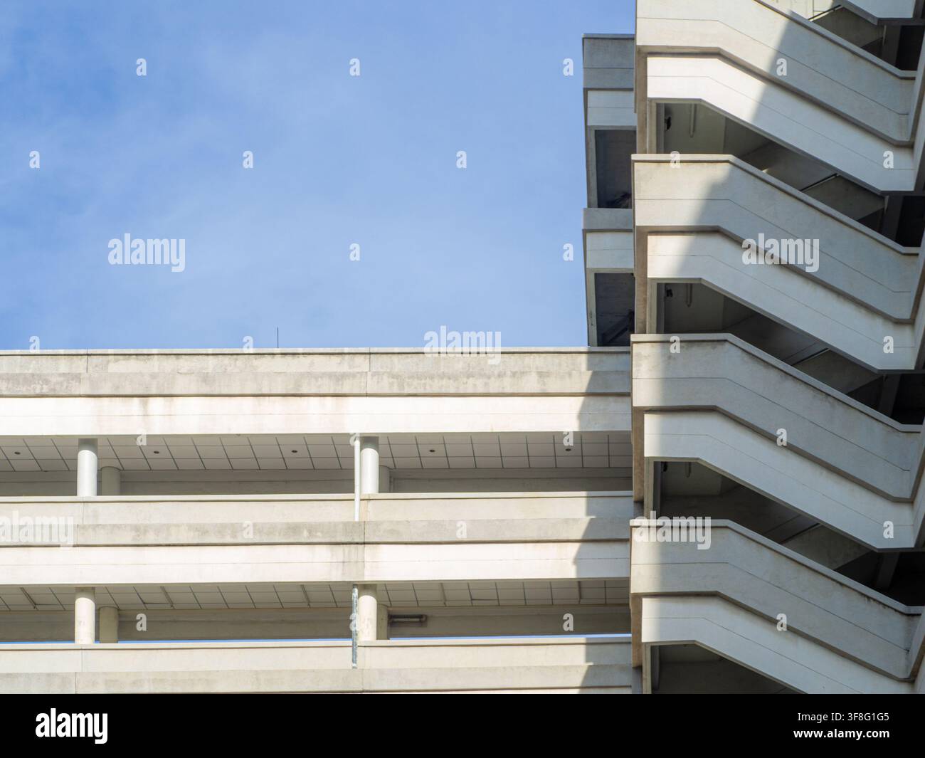 Moderne Betonbaufassade mit Feuerleiter, minimalistischer Architekturstruktur, urbanem Betonwanddesign vor blauem Himmel und Requisite Stockfoto