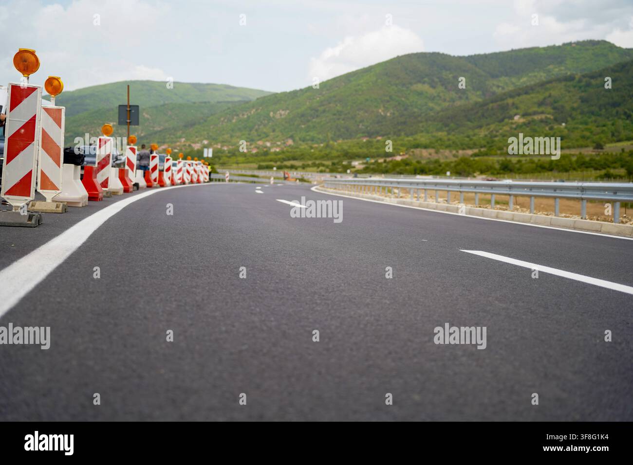 Neu gepflasterte Autobahn durch grüne Berglandschaft mit Baustellen-Sicherheitsbarrieren Stockfoto