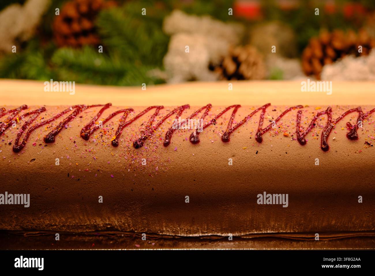 Nahaufnahme eines mit Marmelade verzierten Rollkuchens, mit Kiefernzweigen und Kiefernzapfen im Hintergrund Stockfoto
