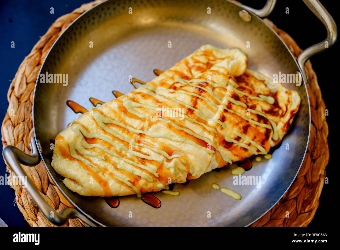 Frisches gefülltes Omelett serviert in einer Metallpfanne mit bunten Saucen in einem Restaurant. Konzept von Frühstück, Komfortessen, Essen und mediterraner Küche Stockfoto