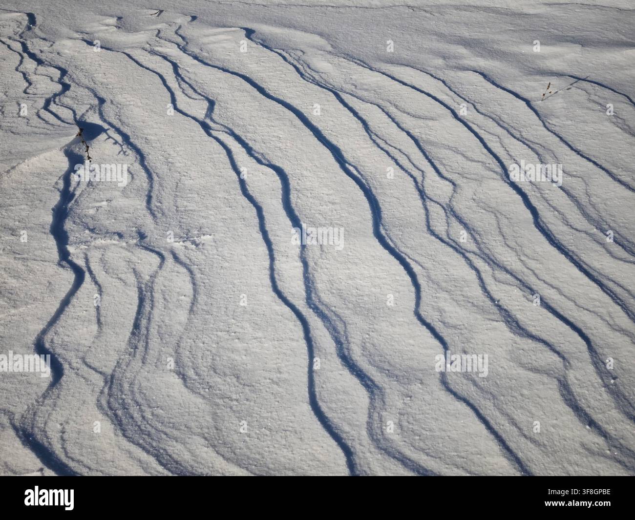 Schnee bildet wellige Linien und Schatten im Sonnenlicht in einem Außenbereich und erzeugt ein strukturiertes Muster auf der Oberfläche. Stockfoto