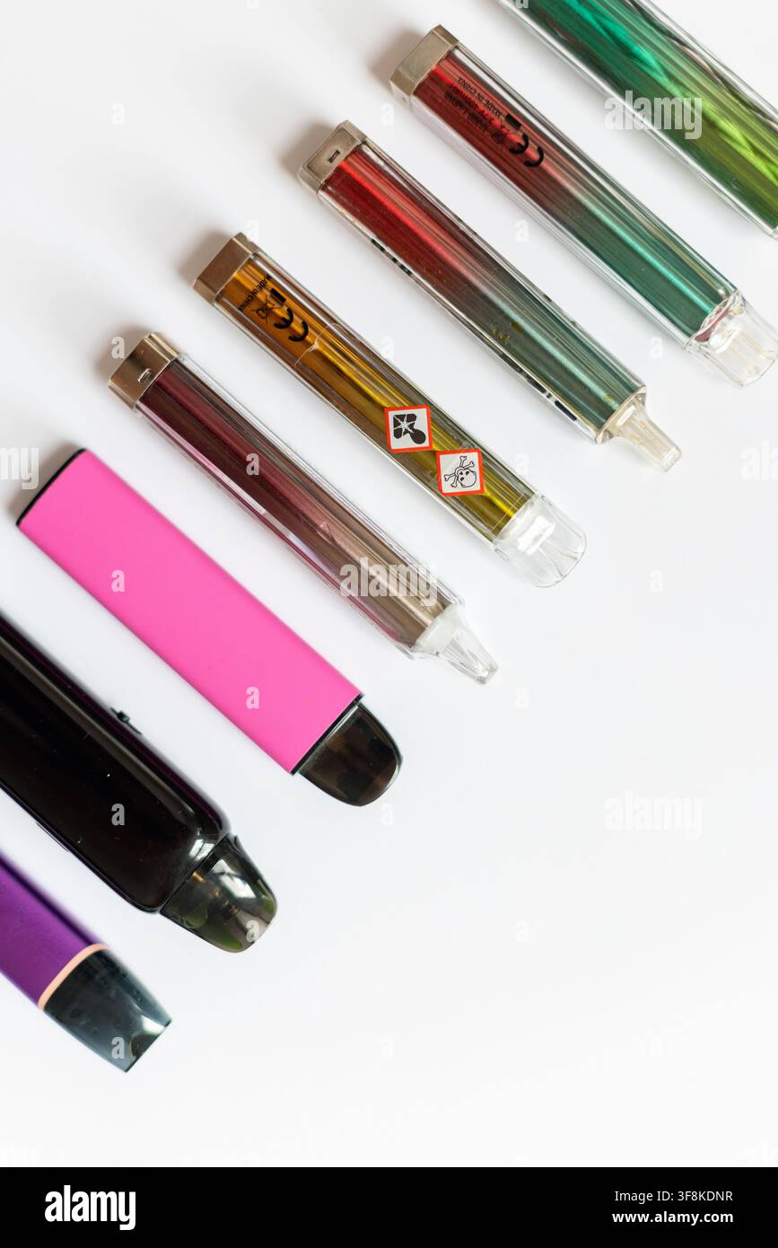 Diagonale Reihe farbenfroher Einweg-E-Zigaretten und Vape-Pods mit toxischen Warnsymbolen, die Nikotinsucht, Gesundheitsgefahren und Wahnsinn repräsentieren Stockfoto