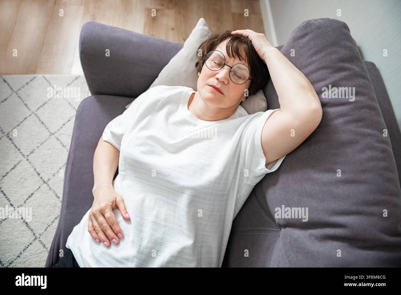 Kranke ältere Frau, die an saisonaler Grippe oder Erkältung leidet und auf dem Sofa liegt. Kranke Seniorin fühlt sich mit Influenza zu Hause unwohl Stockfoto