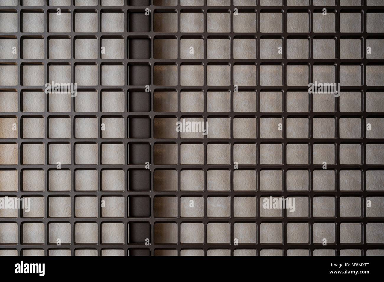 Abstraktes geometrisches Muster eines dunklen Metallgitterbildschirms über einer texturierten beigen Wand. Stockfoto