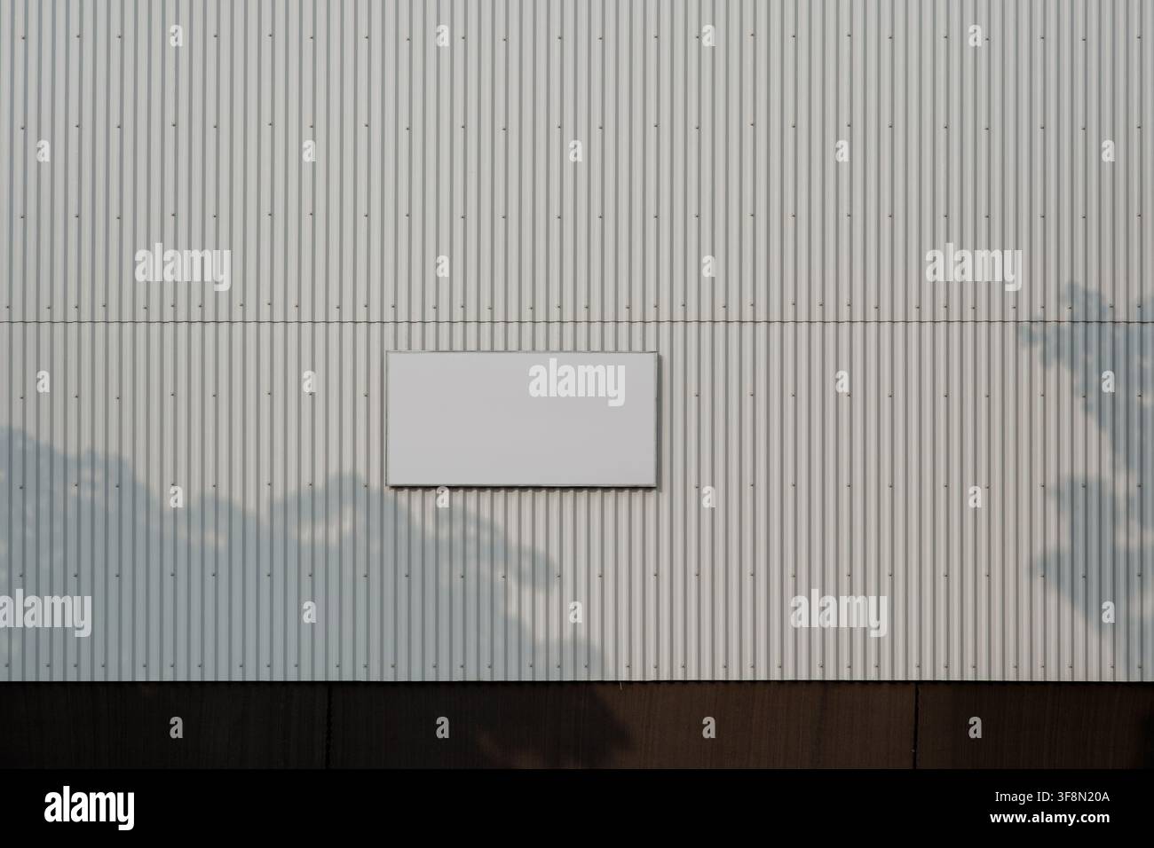Leeres weißes Schild an einer wellblechverkleideten Wand mit Schatten von Baumblättern. Stockfoto